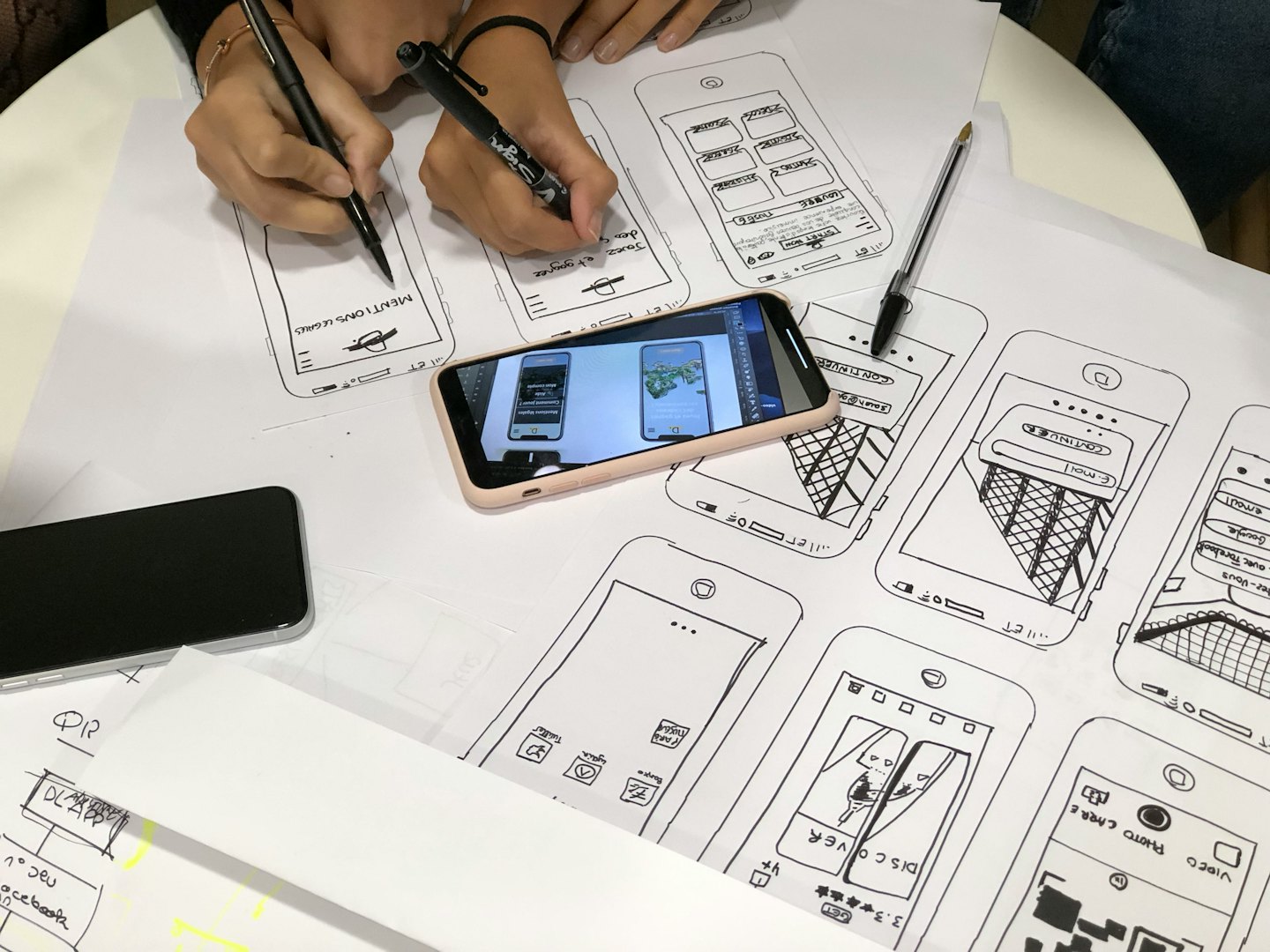 Hands drawing mobile app wireframes on paper at a table.